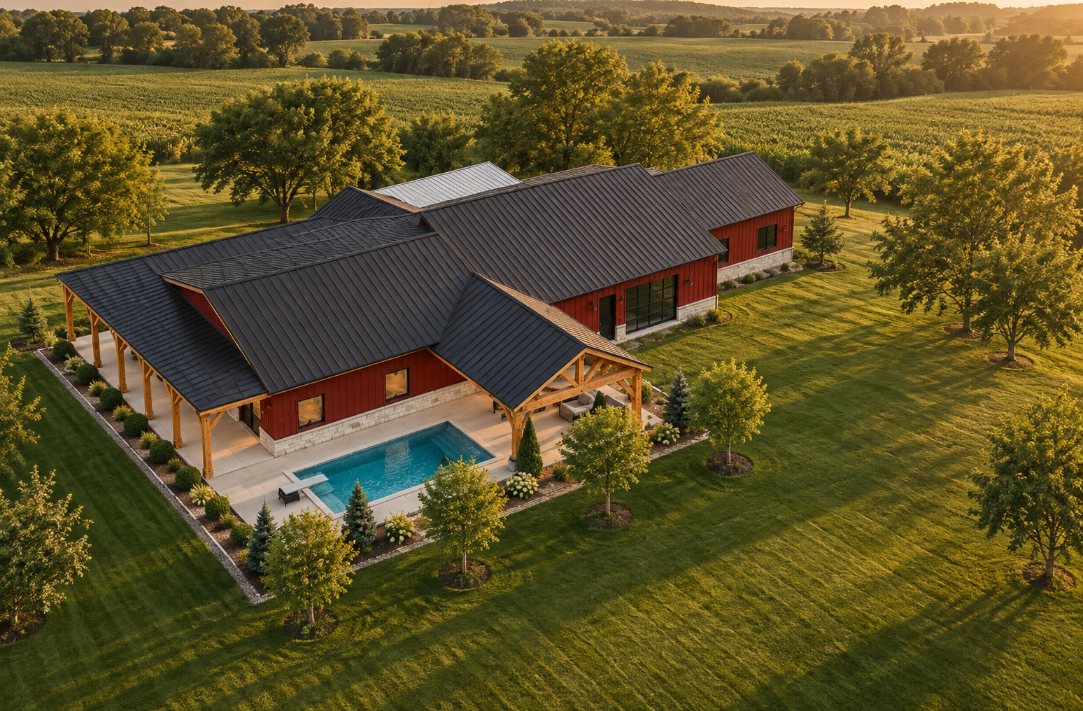 Aerial view of a red country barndominium with a pool and surrounding fields